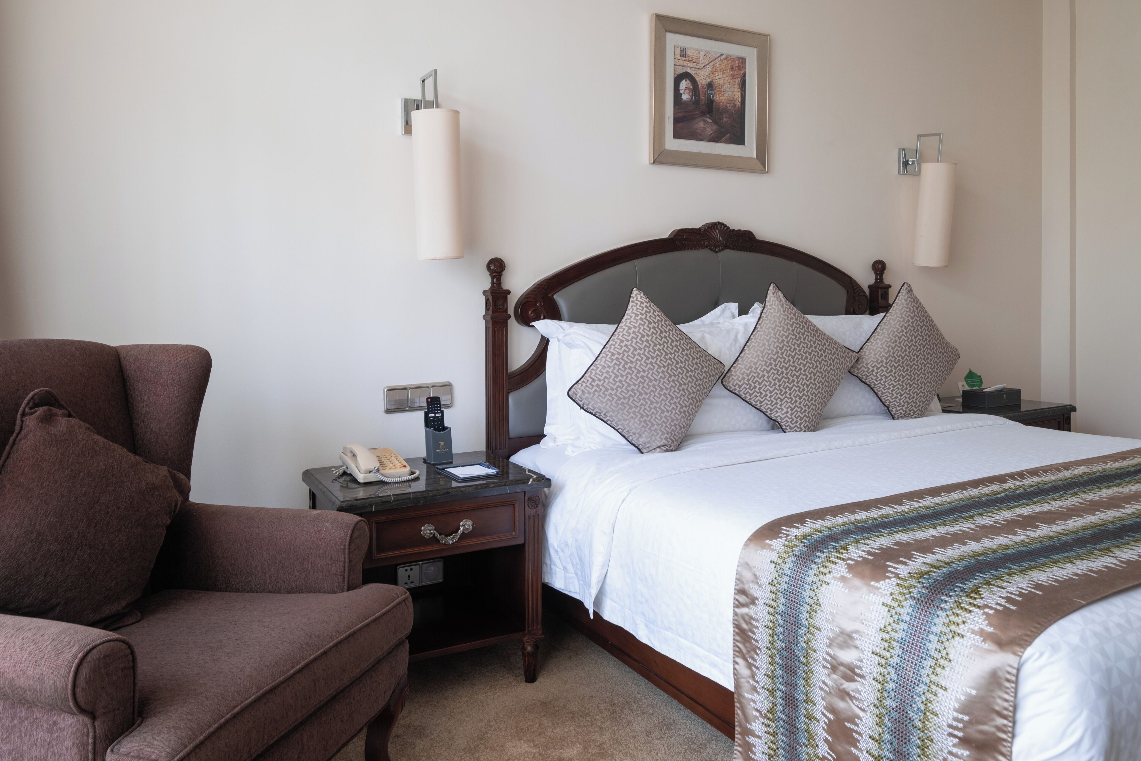 Una habitación de hotel con una cama, una silla, una mesita de noche y una lámpara fijada a la pared.