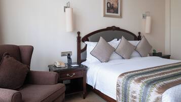 Una habitación de hotel con una cama, una silla, una mesita de noche y una lámpara fijada a la pared.