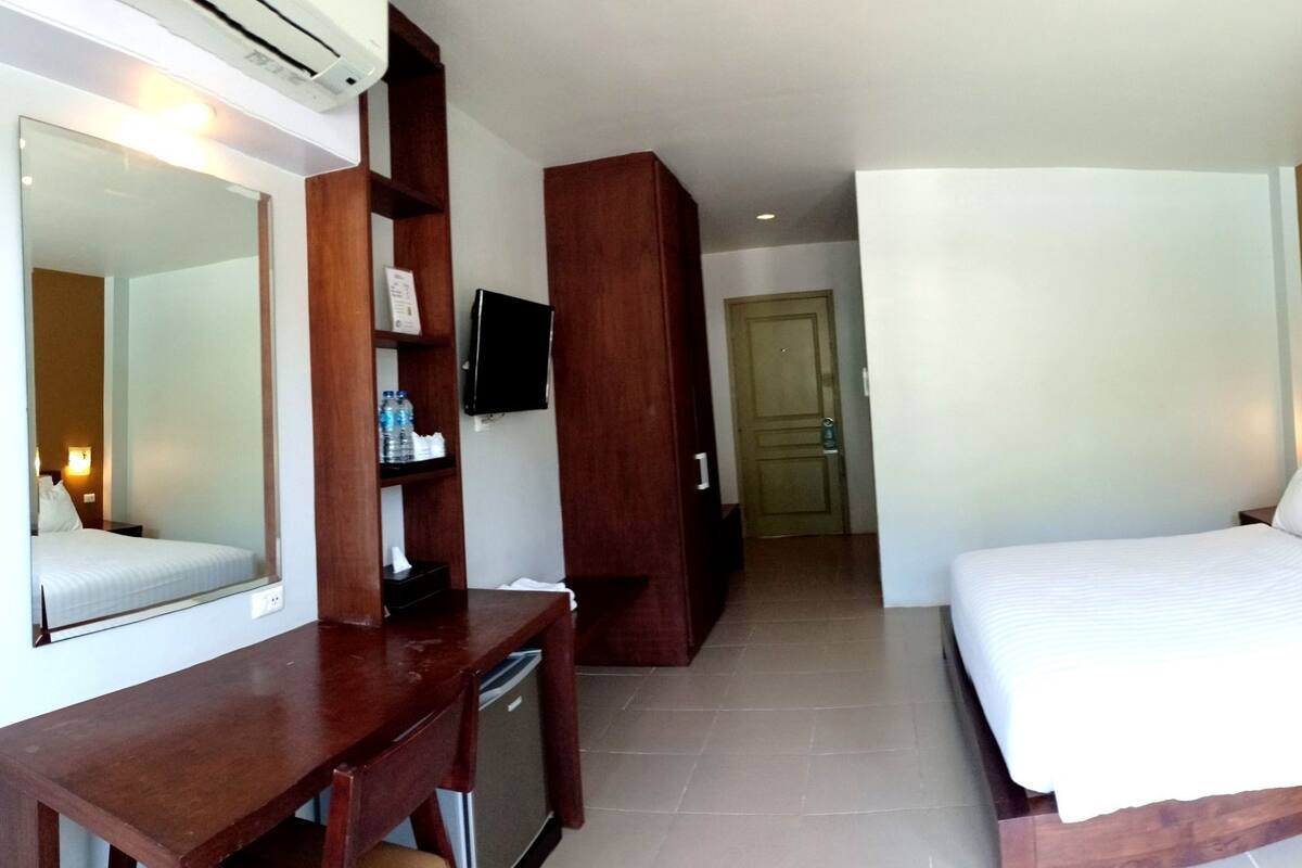 Habitación de hotel con una cama grande, un escritorio, una silla, un televisor y una mesita de noche.