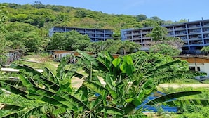 Ein Hotel mit mehreren Etagen und Balkonen, umgeben von üppiger Vegetation und Hügeln.