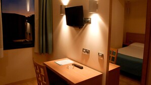 A hotel room with a desk, a television mounted on the wall, a bed with a green bedspread, and a mirror reflecting part of the room. - Hostal Aralar (Berrioplano)