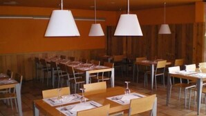 A restaurant with multiple tables and chairs, white pendant lights, and wooden walls. - Hostal Aralar (Berrioplano)