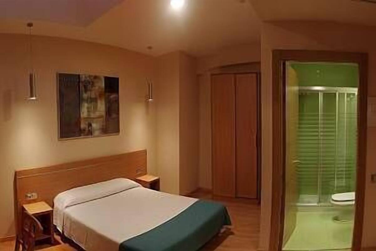 Habitación de hotel con cama, escritorio, armario y baño visible a través de una puerta abierta.