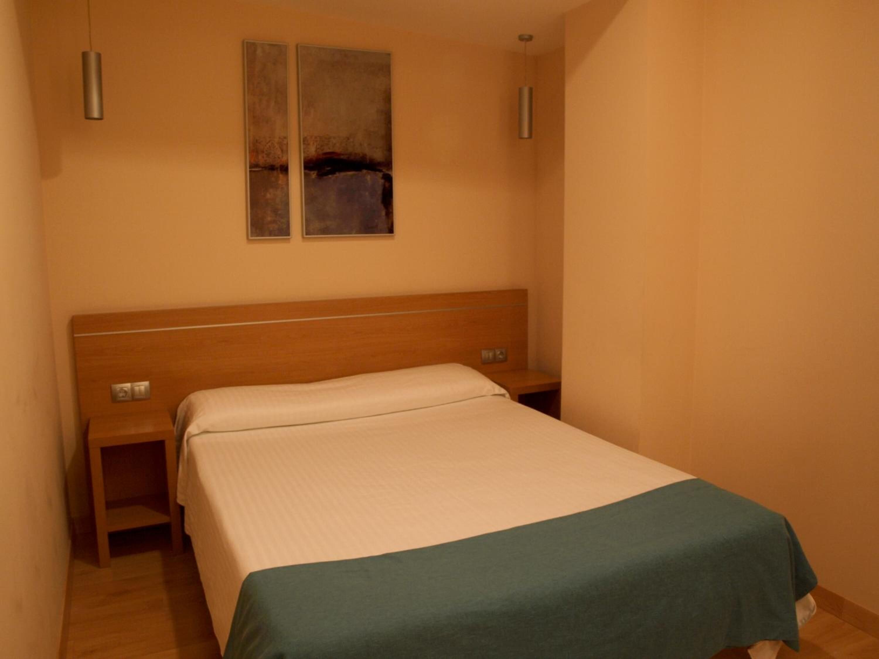Une chambre d’hôtel avec une tête de lit en bois, un lit simple, une table de chevet et une œuvre d’art accrochée au mur.