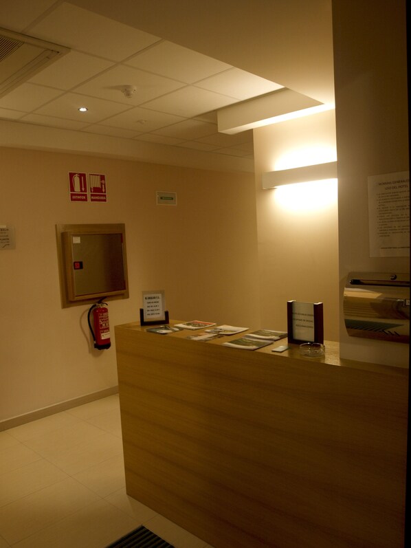 Un mostrador de recepción de hotel con un extintor, un espejo y carteles informativos en la pared.