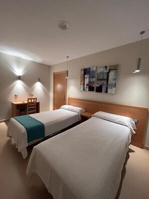 A hotel room with two beds, a desk, and a chair.