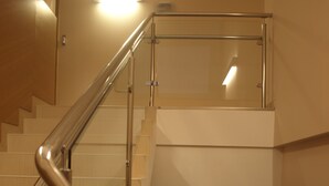 A staircase with a metal handrail and wooden steps, leading to a landing with a glass railing. - Hostal Aralar (Berrioplano)