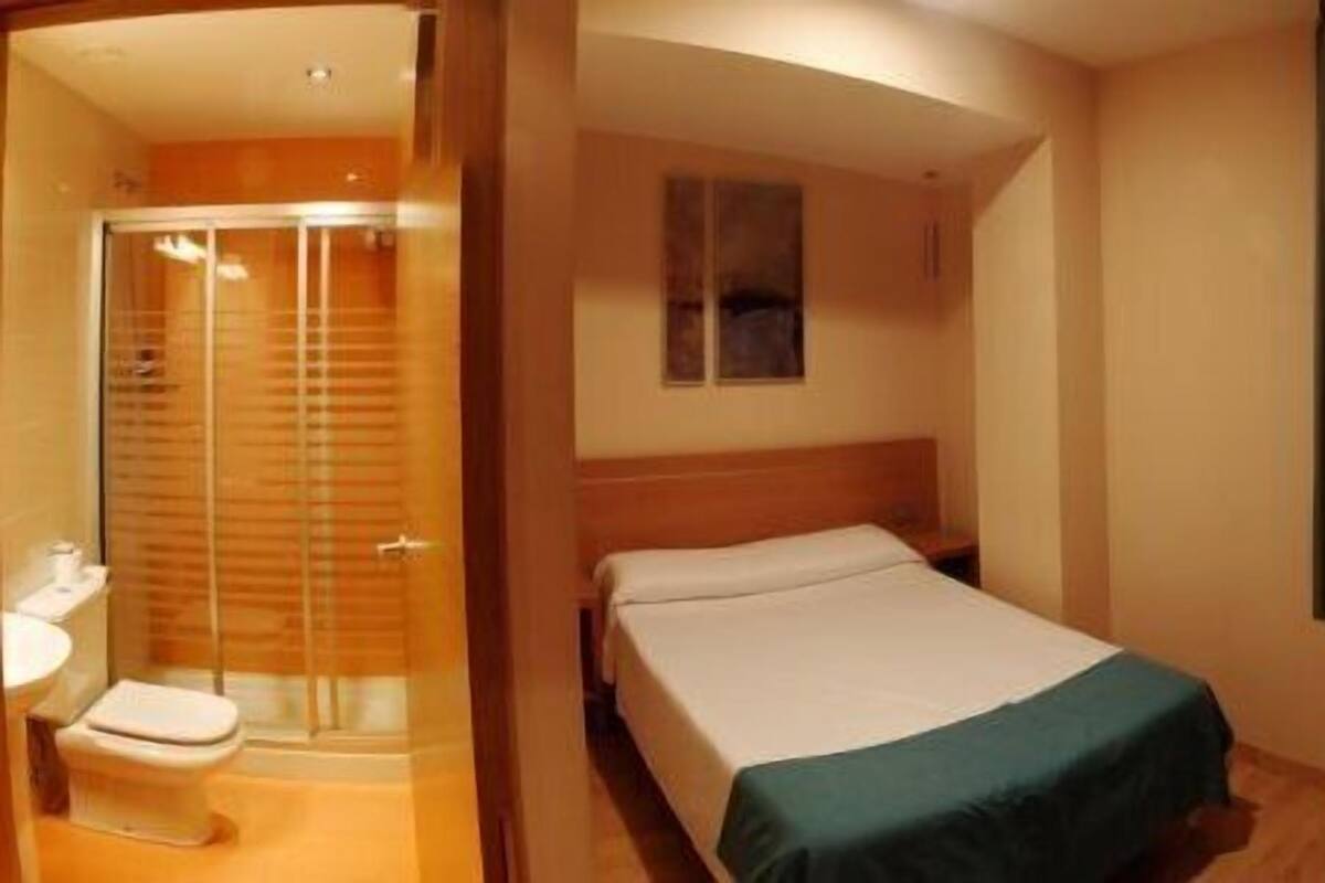 Una habitación de hotel con cama, ventana con vistas, zona de ducha y una pequeña mesa.