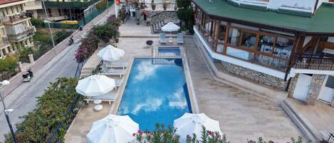 A swimming pool with lounge chairs and umbrellas, a stone wall, and a building with a green roof.