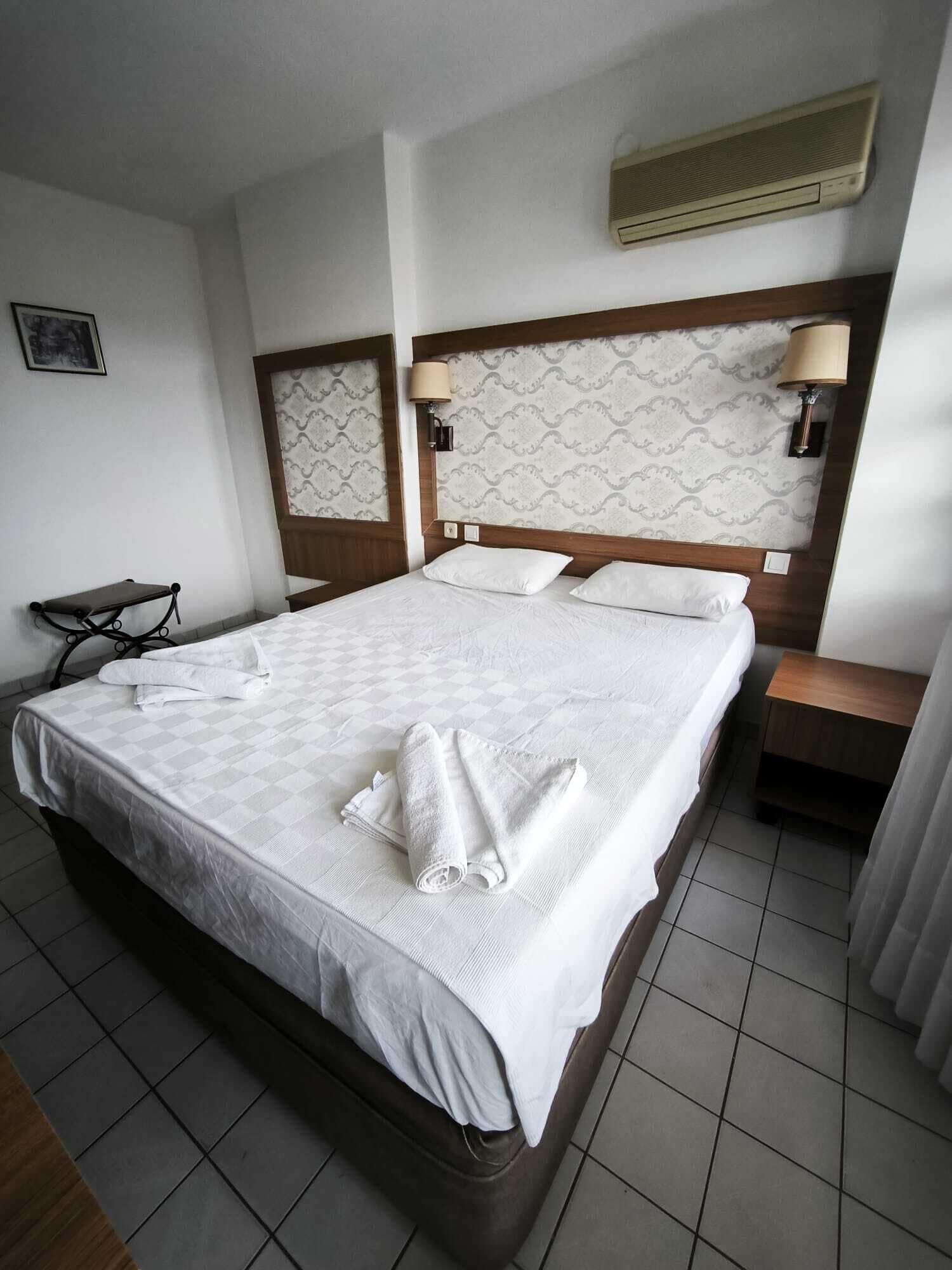 Ett hotellrum med en stor säng, två sänglampor, ett litet bord och en luftkonditioneringsanläggning.