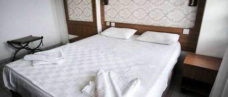 Ett hotellrum med en stor säng, två sänglampor, ett litet bord och en luftkonditioneringsanläggning.