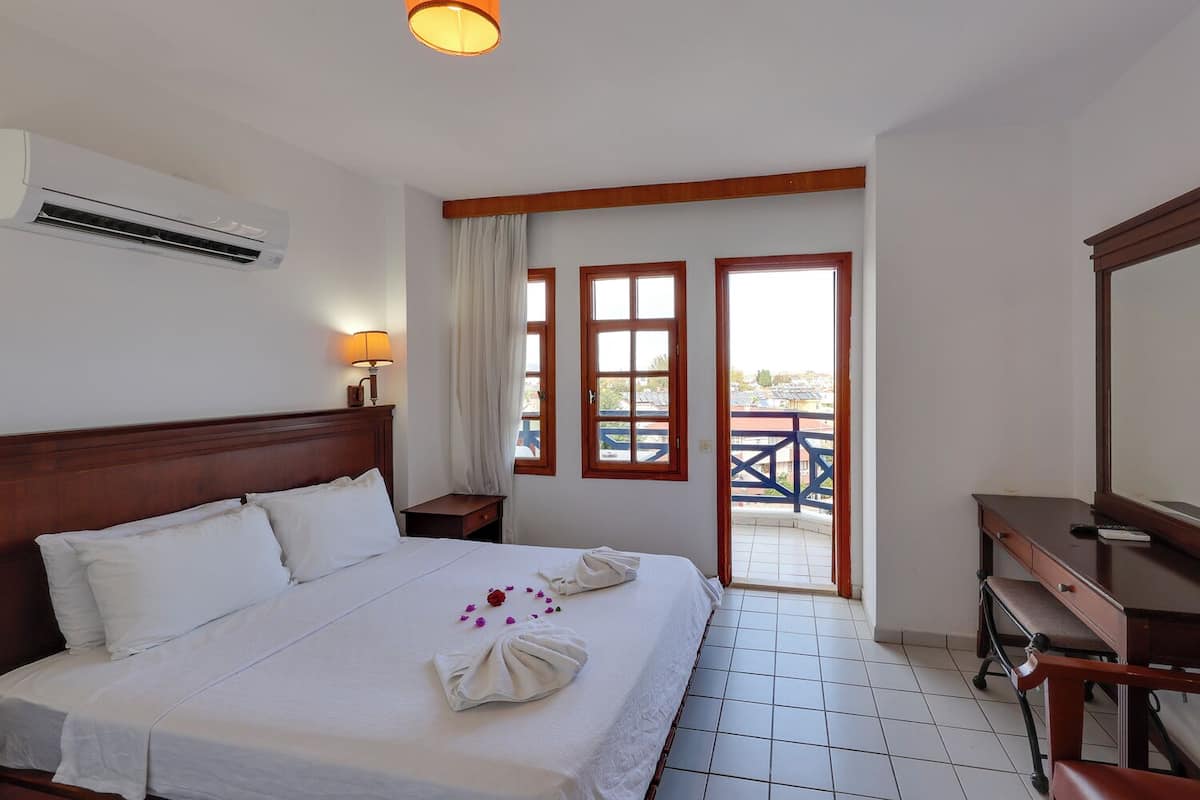 Habitación de hotel con cama, escritorio, aire acondicionado, lámpara y vistas por una puerta.