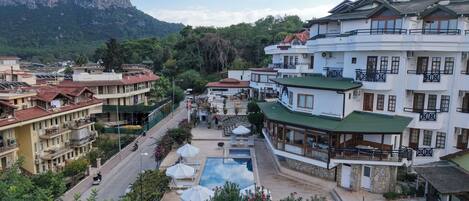 Un hotel con piscina, balcones y montañas al fondo.