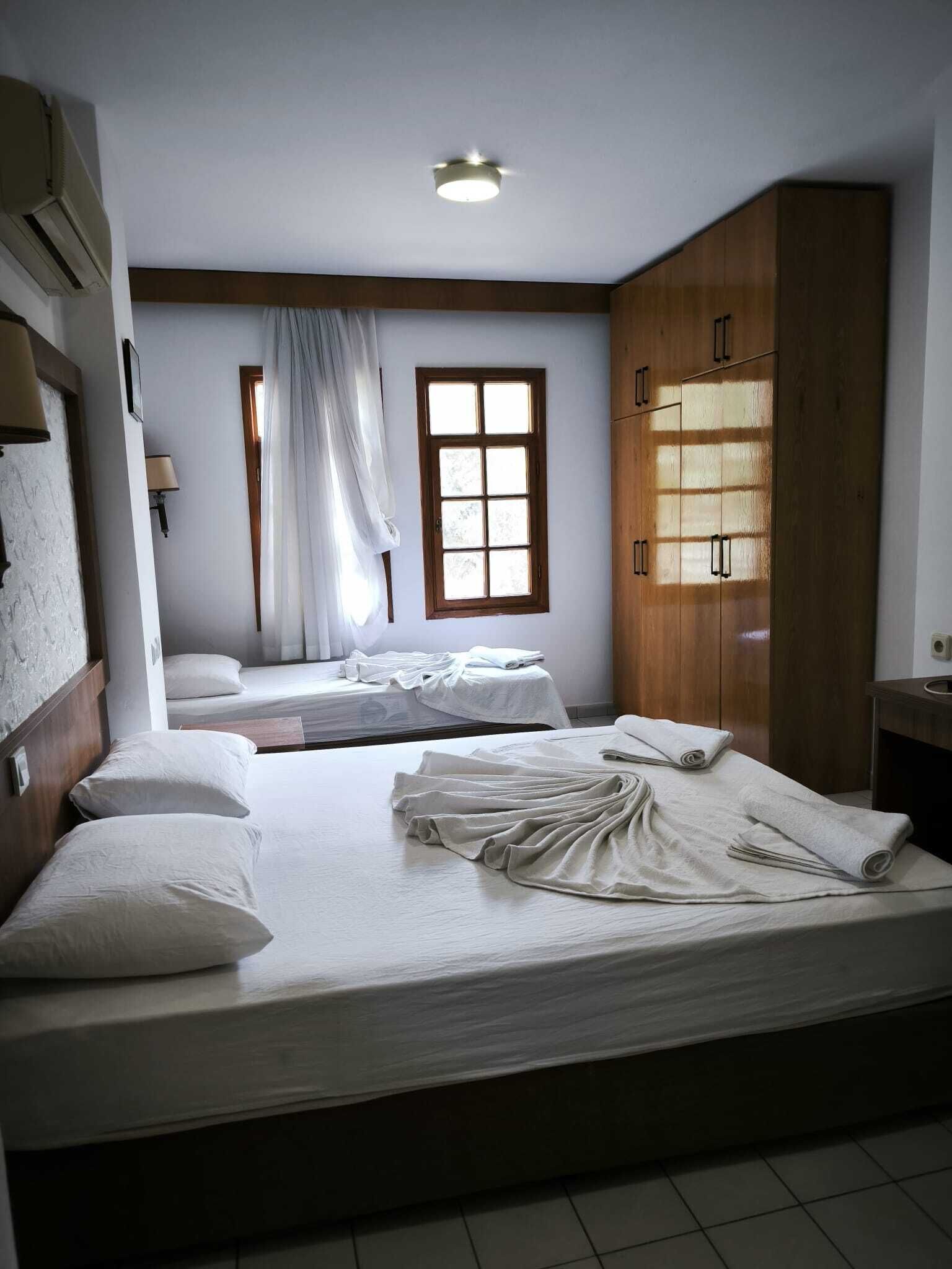 A hotel room with two beds, a window with curtains, a wooden wardrobe, and a ceiling light.