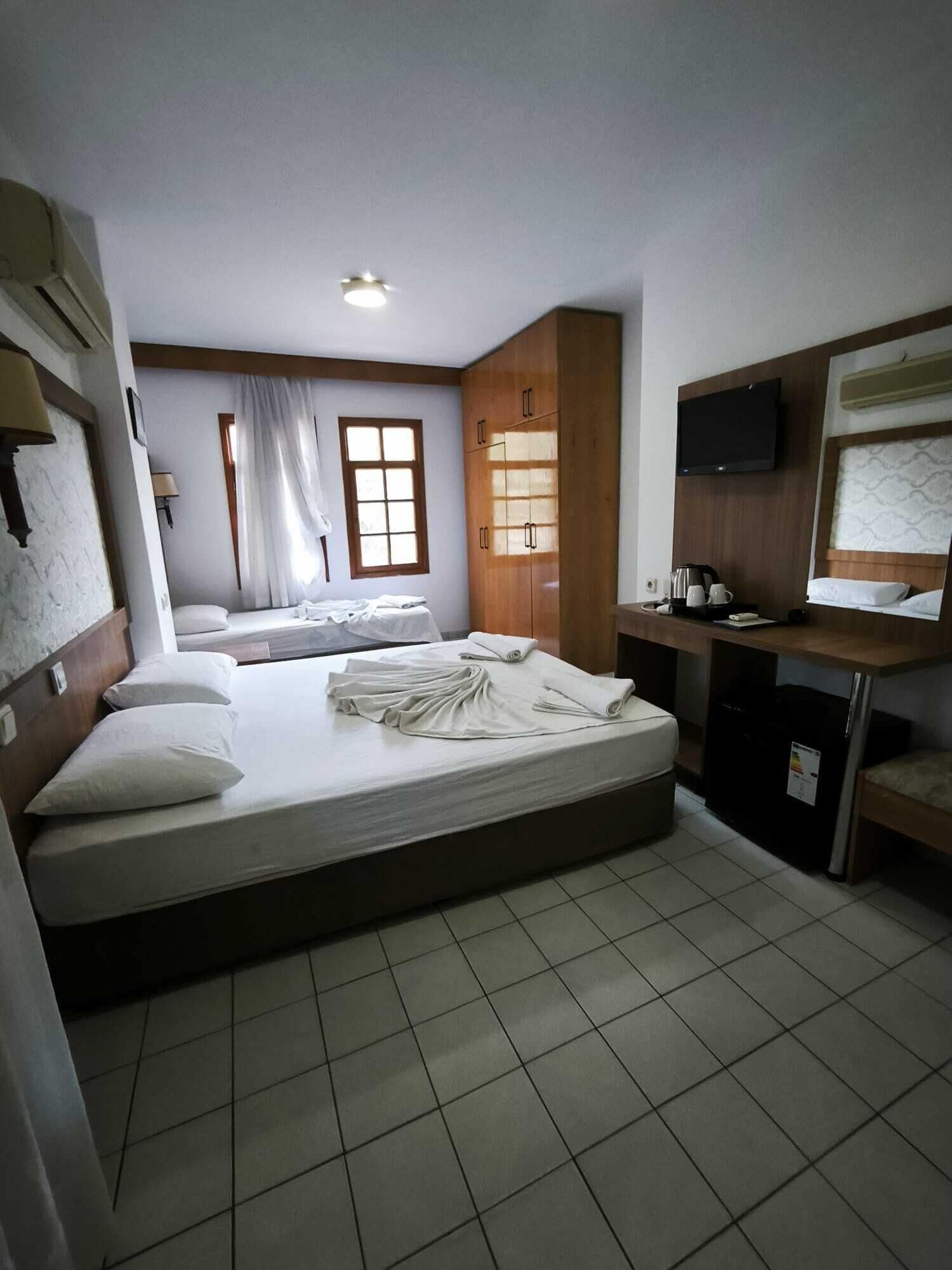 Ein Hotelzimmer mit einem großen Bett, einem Schreibtisch mit Fernseher, einem Fenster mit Vorhängen und einem Kleiderschrank.