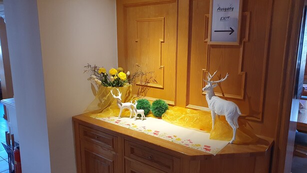 A wooden cabinet with a sign indicating an exit, a vase with yellow flowers, and deer figurines. - Gasthaus Brauner Hirsch (Hann. Muenden)