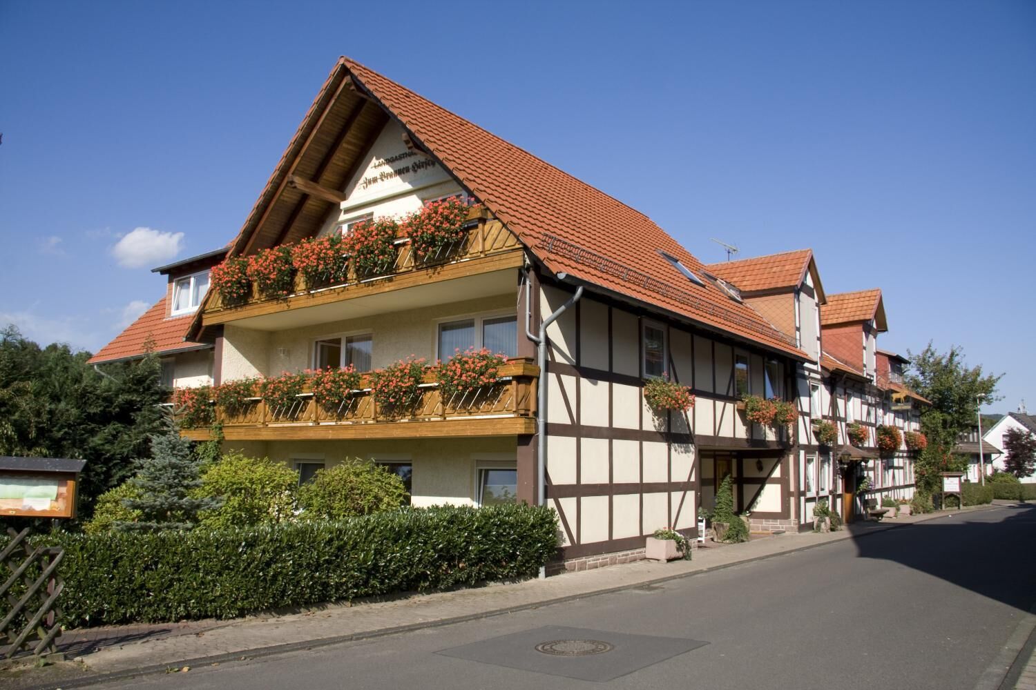Ein traditionelles Fachwerkhäuschen mit Balkonen, die mit Blumen geschmückt sind, unter wolkenlosem Himmel und einer gepflegten Straßenbegrenzung.