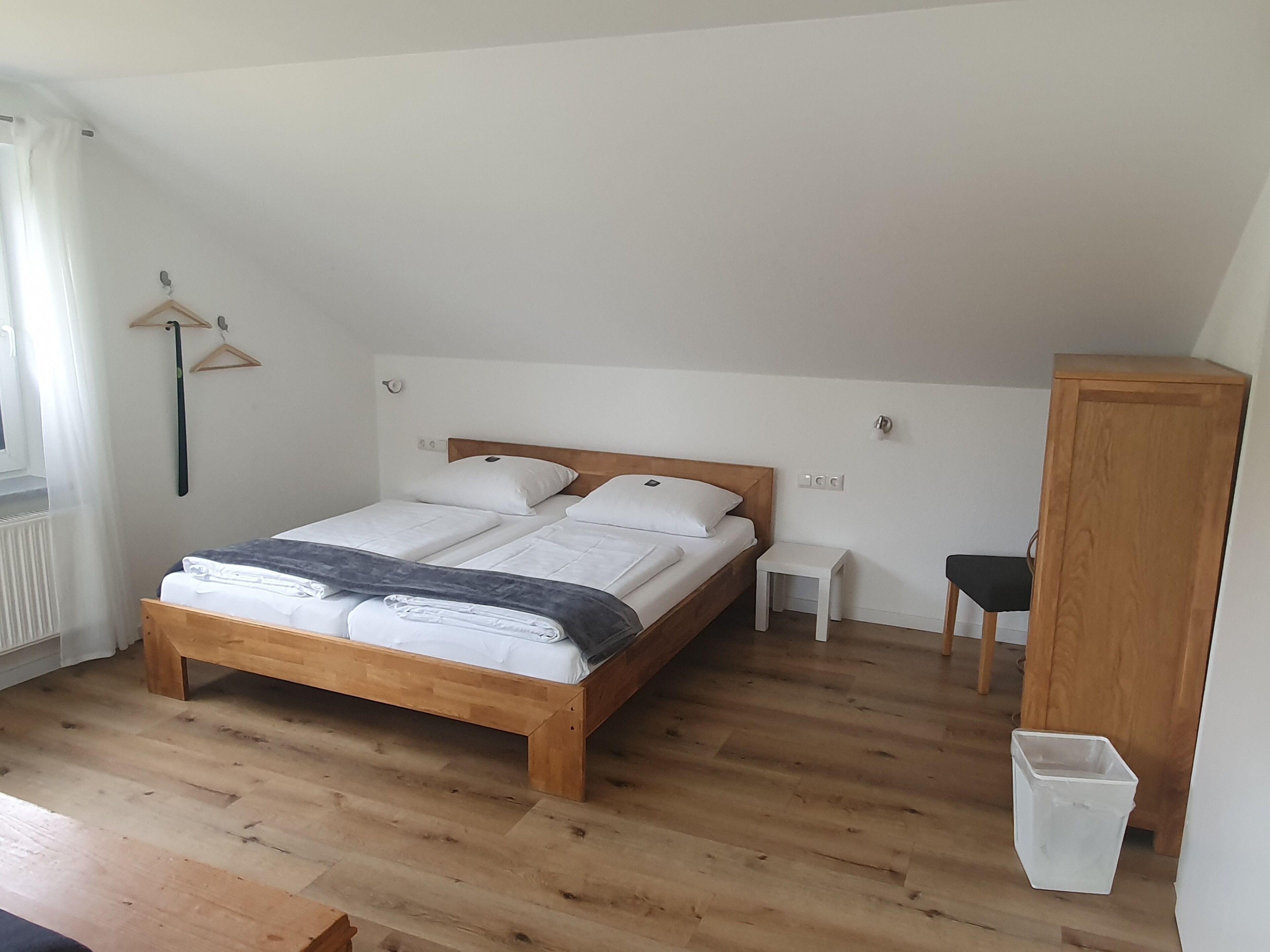 A bedroom with a wooden bed, a small bedside table, a nightstand, a wooden wardrobe, and a radiator.