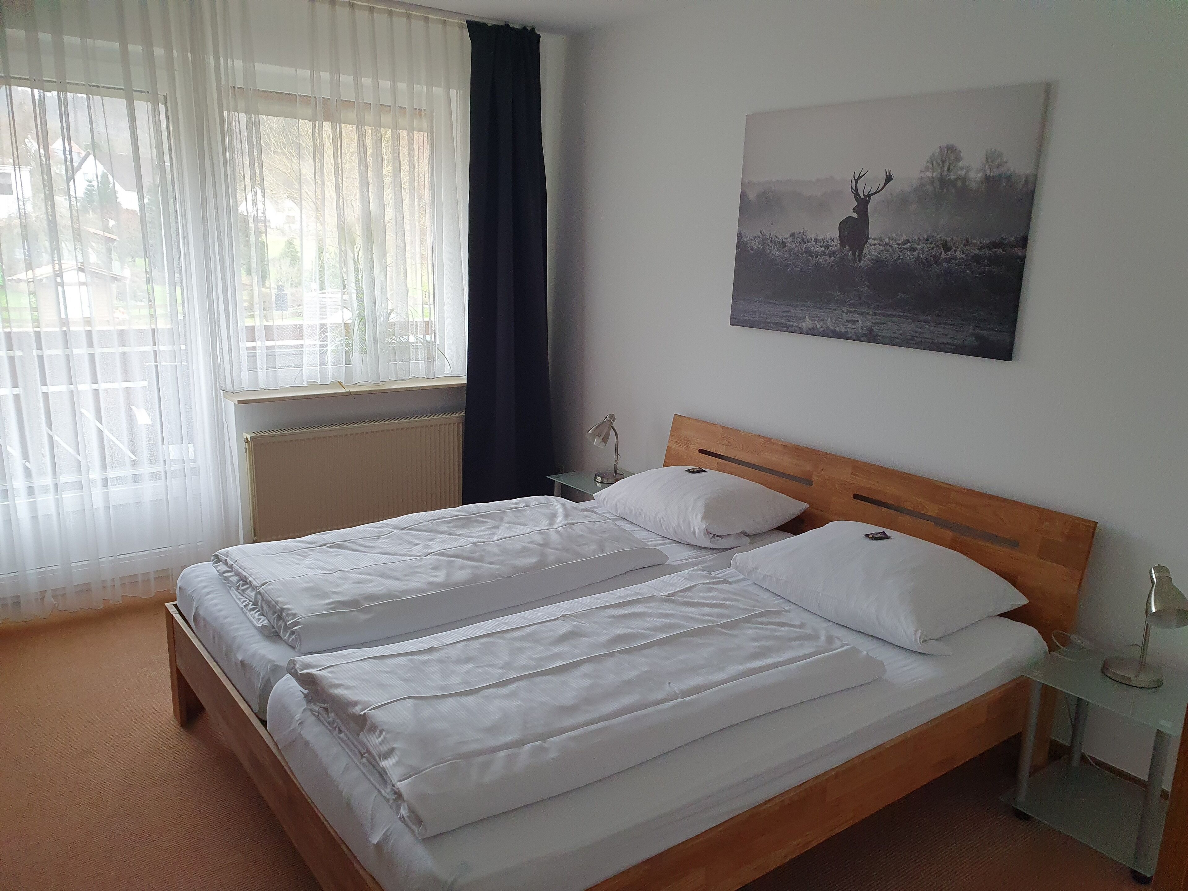 Ein ordentlich bezogenes Doppelbett mit weißen Leinentüchern, ein Holzkopfschild und ein Nachttisch mit Lampe.