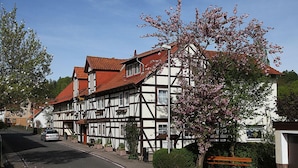 A traditional half-timbered building with a red-tiled roof, a bench, and a flowering tree in front. - Gasthaus Brauner Hirsch (Hann. Muenden)