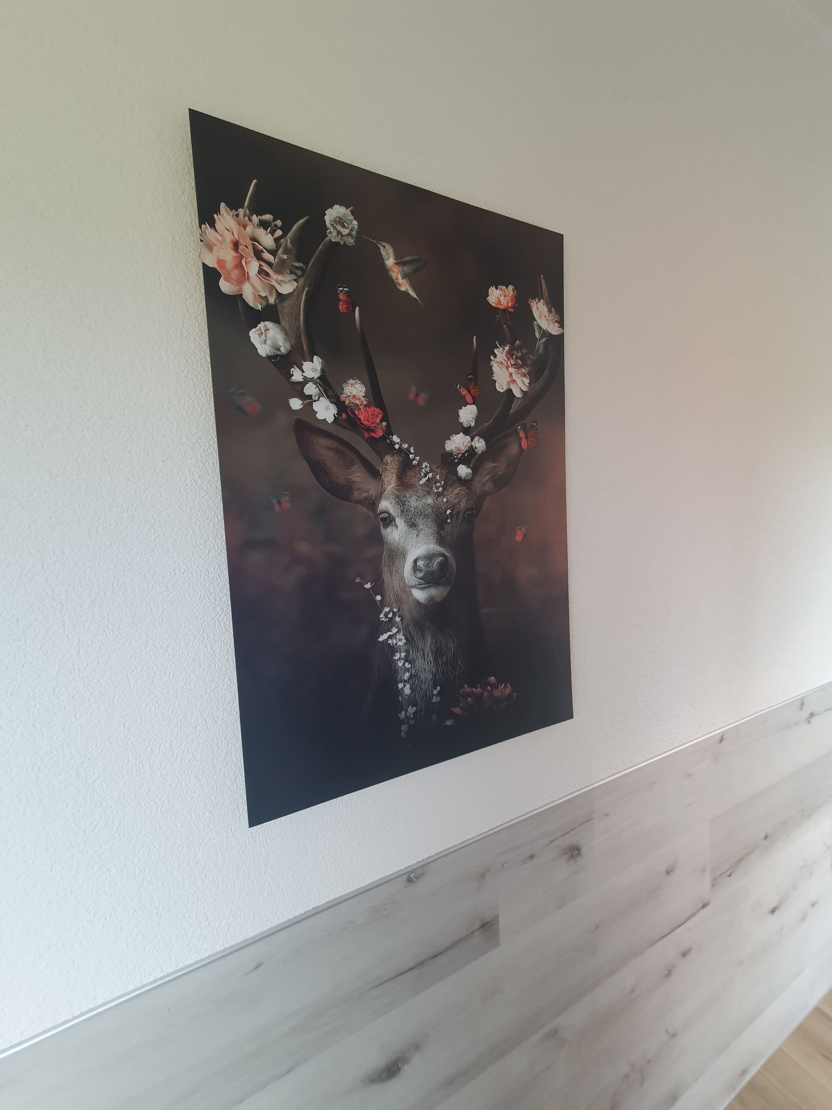 A wall-mounted painting of a deer with antlers adorned with flowers.