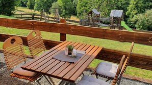 A wooden deck with a table and chairs, overlooking a playground and lush greenery. - Gasthaus Brauner Hirsch (Hann. Muenden)