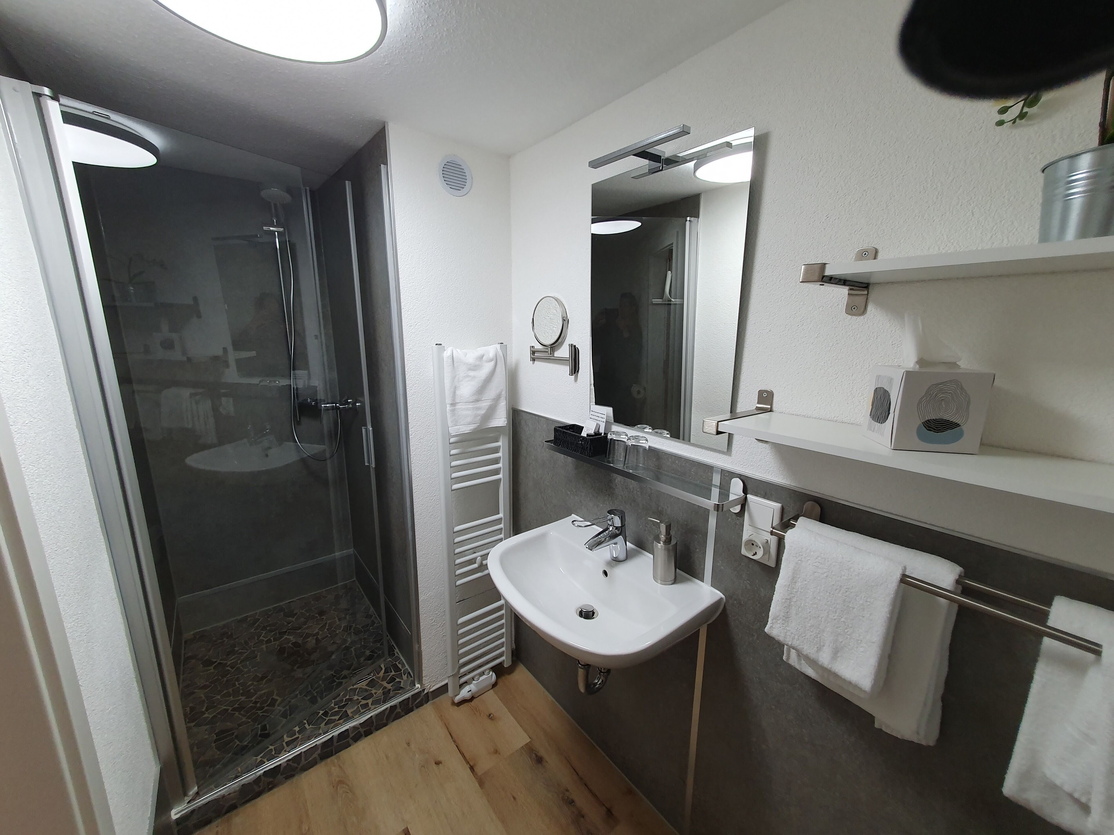 Ein modernes Badezimmer mit einer gläsernen Duschkabine, einem weißen Waschbecken und einem Spiegel darüber.