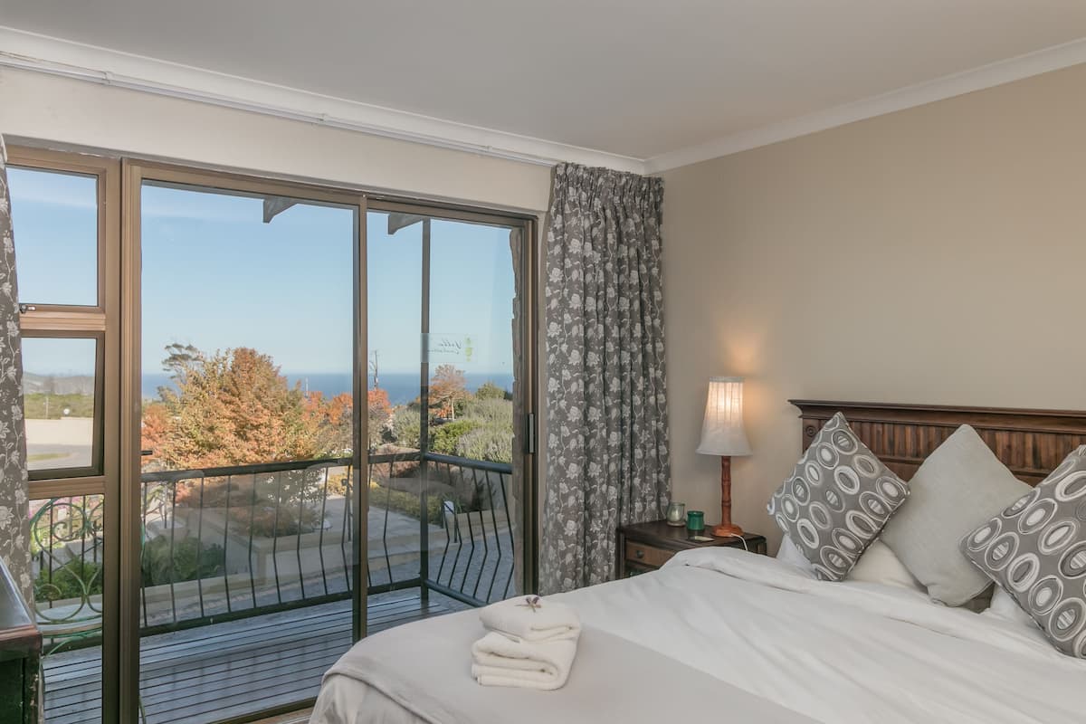 A bedroom with a large sliding glass door leading to a balcony, a bed with white linens, patterned pillows, and a nightstand with a lamp.