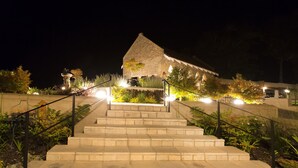 A stone staircase leading to a building with a thatched roof, surrounded by well-lit plants and a small fountain. - Villa Castollini (Knysna)