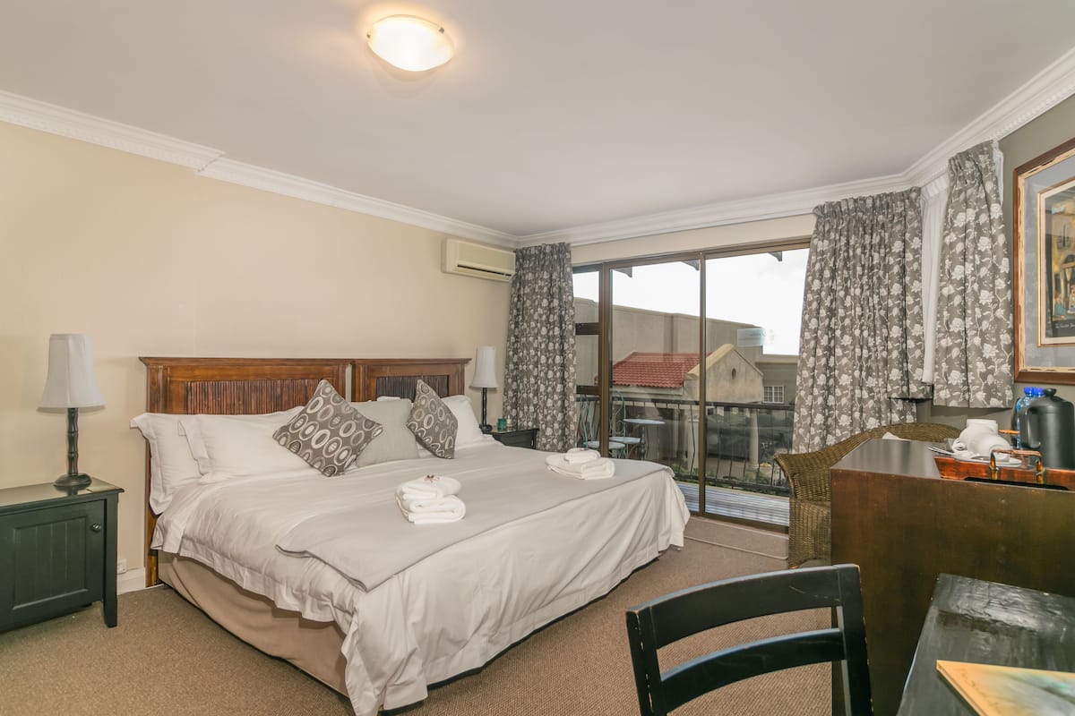 A hotel room with a large bed, a desk, a chair, a lamp, and a view of the outside.