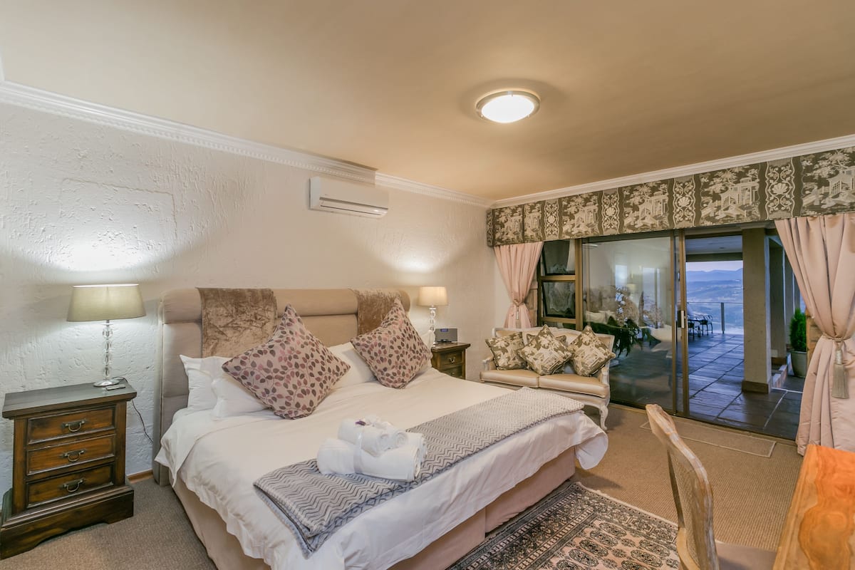 A bedroom with a large bed, a nightstand, a chair, and a view of the outdoors through a glass door.