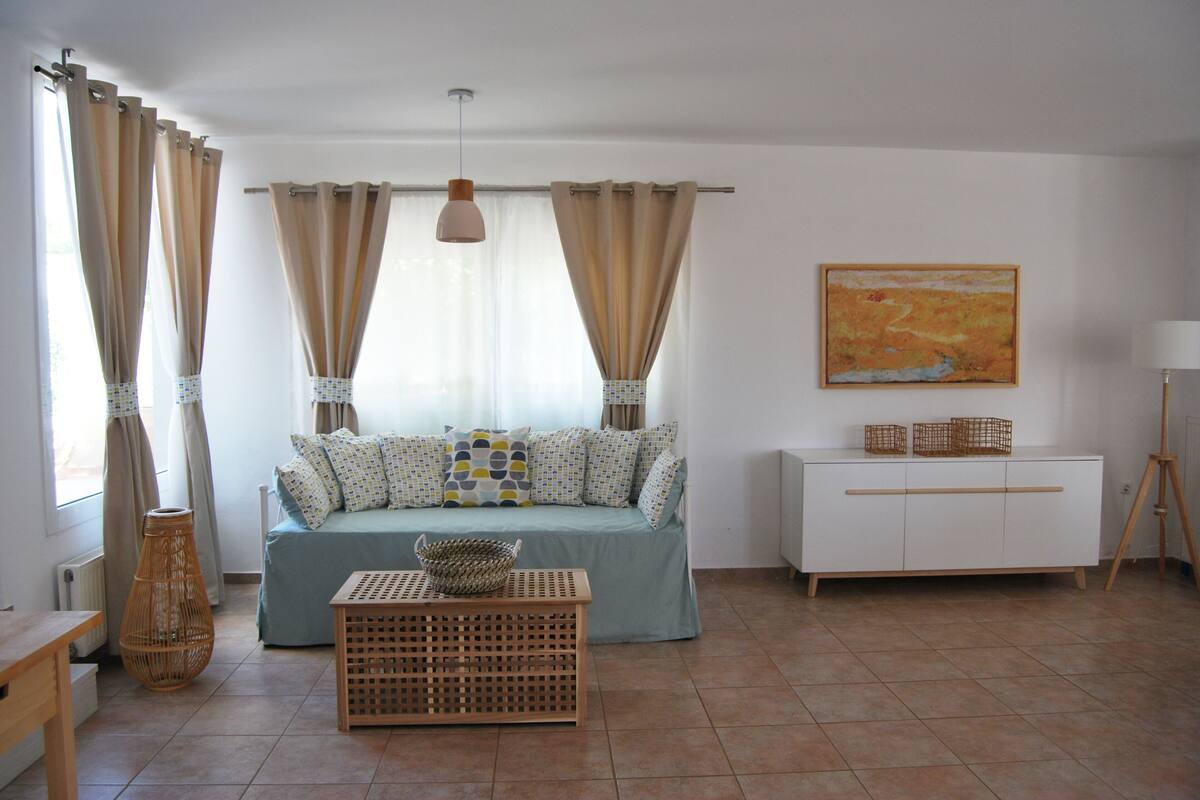 A living room with a sofa, a side table, a lamp, a painting, and a window with curtains.