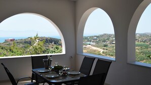 Un coin repas avec une table dressée pour quatre personnes, de grandes fenêtres en arc offrant une vue sur un paysage côtier.