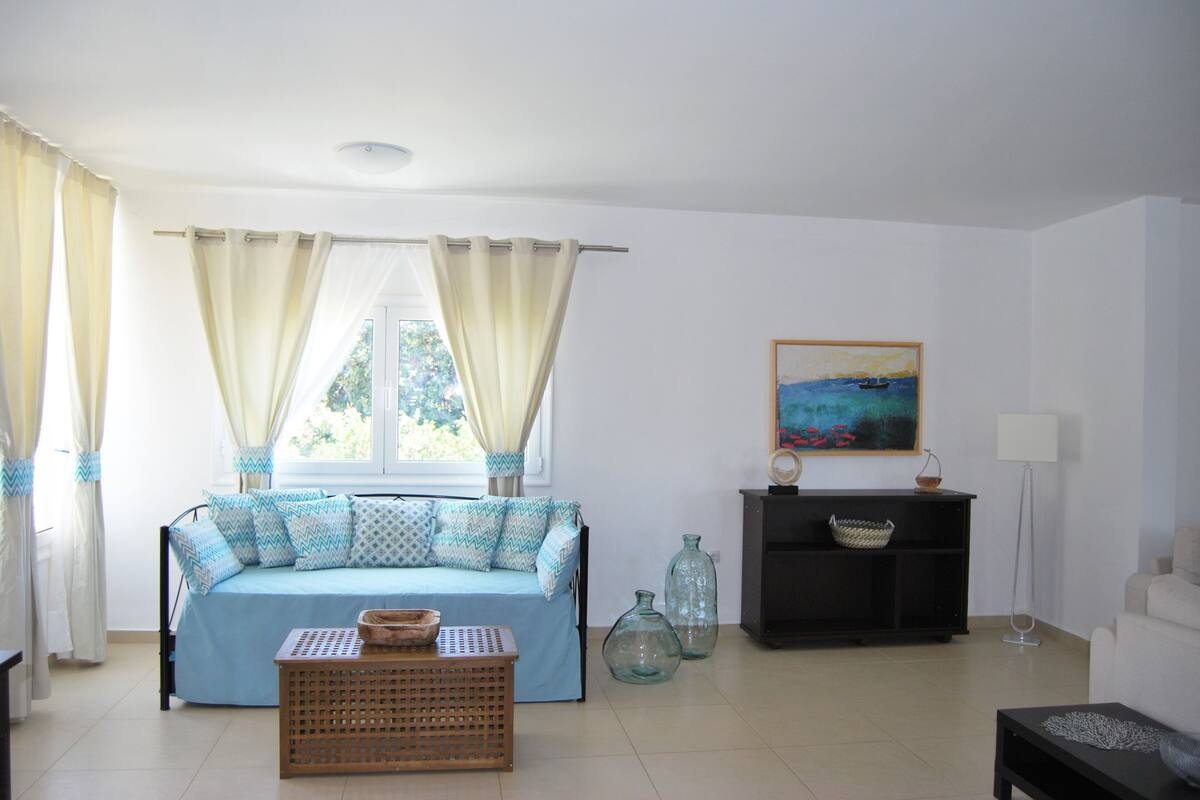 A bedroom with a bed, curtains, a painting, a lamp, and a small table.