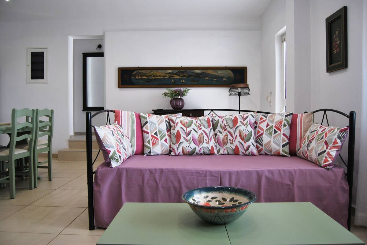 A living room with a sofa, a table with a bowl, and a painting on the wall.