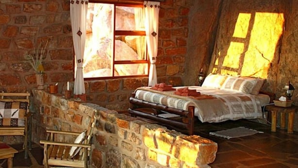 Un dormitorio rústico con paredes de piedra, una cama, una silla de madera y una mesita.