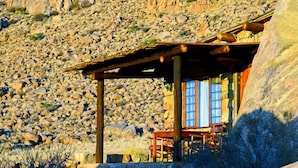 Una cabaña rústica con pared de piedra, vigas de madera y una mesa con sillas.