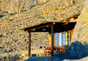 Una cabaña rústica con pared de piedra, vigas de madera y una mesa con sillas.