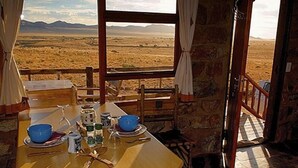 Un comedor rústico con una mesa dispuesta para dos personas, vista a un paisaje extenso a través de una ventana y paredes de piedra.