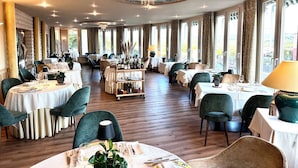 Un restaurante con mesas redondas, sillas tapizadas en verde y un techo decorativo.