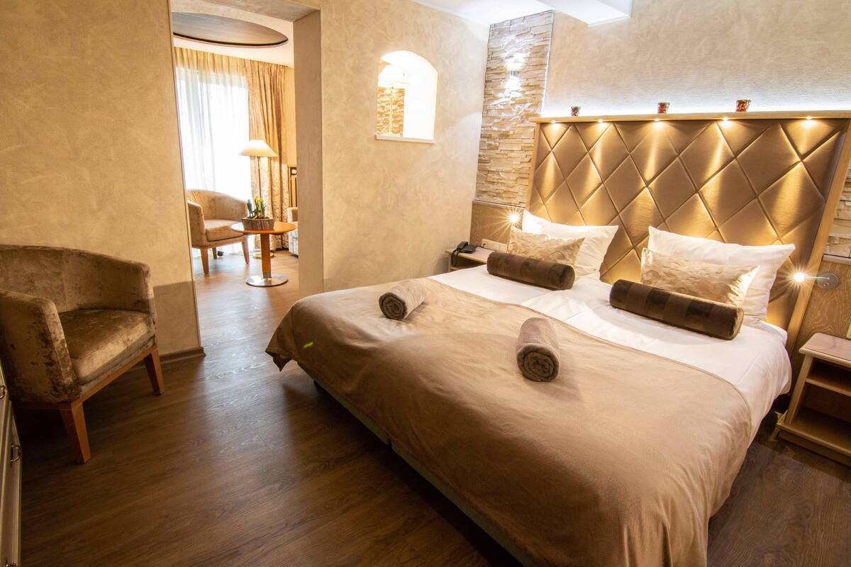 Une chambre d’hôtel avec un grand lit, une tête de lit dotée d’un éclairage intégré, une petite table et une chaise.