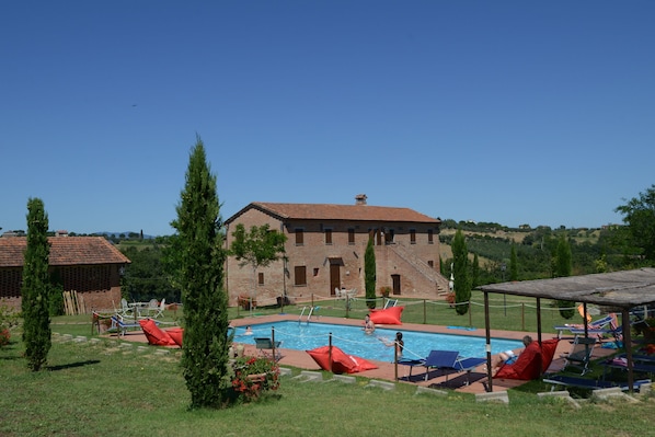 A pool area with lounge chairs, a brick building, and a clear sky.
