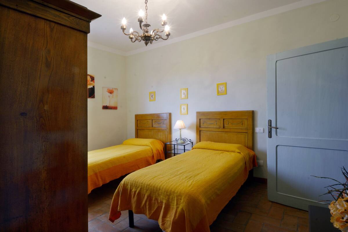 A room with two beds, a wooden wardrobe, a chandelier, and a door.