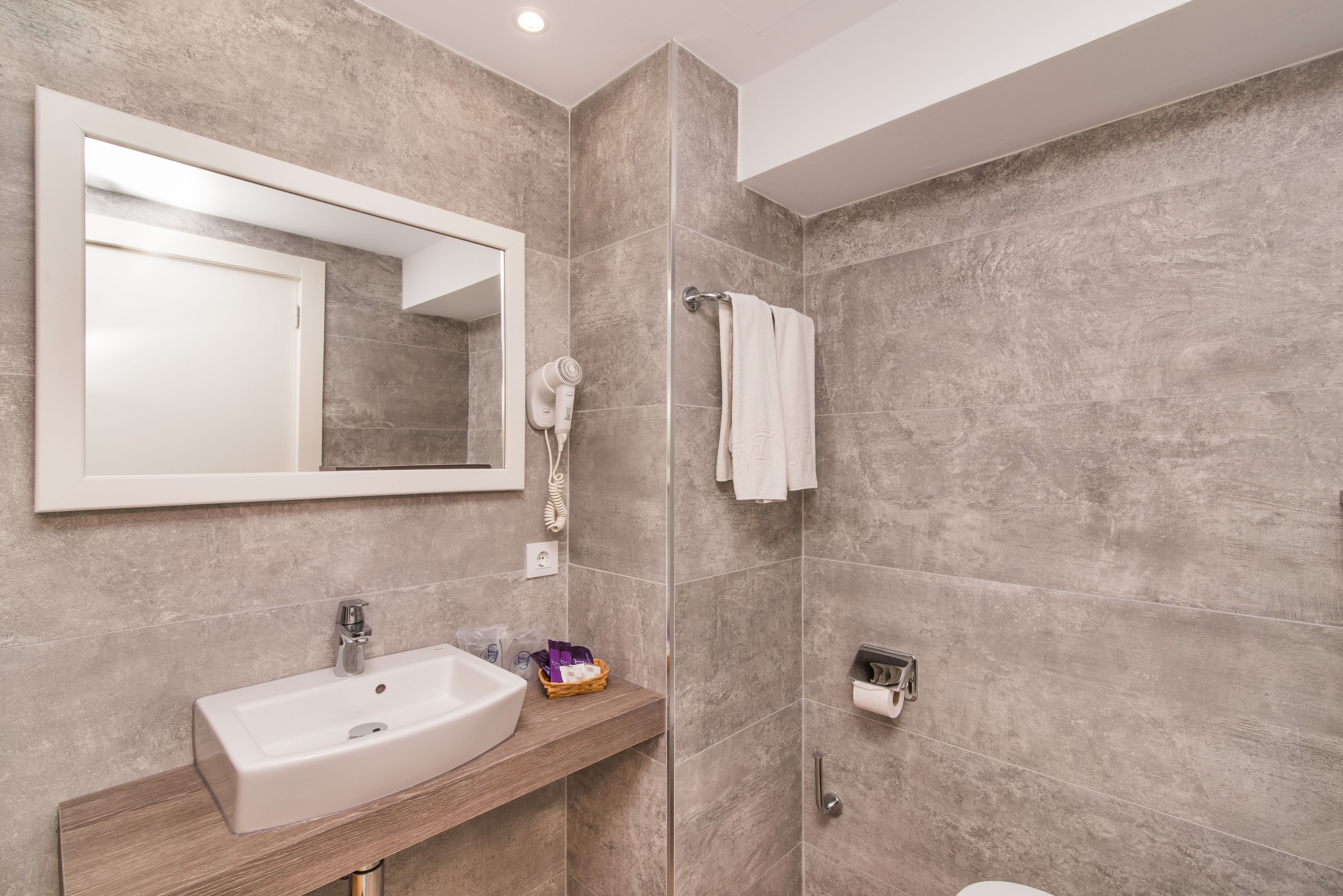 Un baño moderno con un espejo grande, un lavamanos, un perchero para toallas y una zona de ducha.