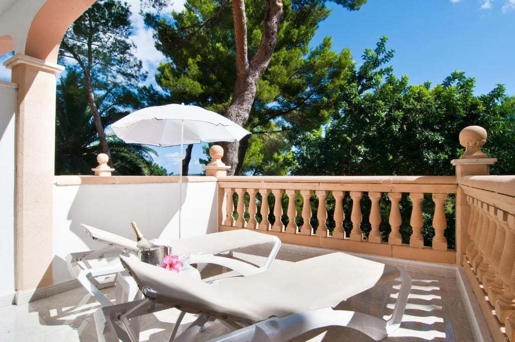 Ein Balkon mit weißen Liegestühlen, einem weißen Sonnenschirm und einer dekorativen Brüstung.