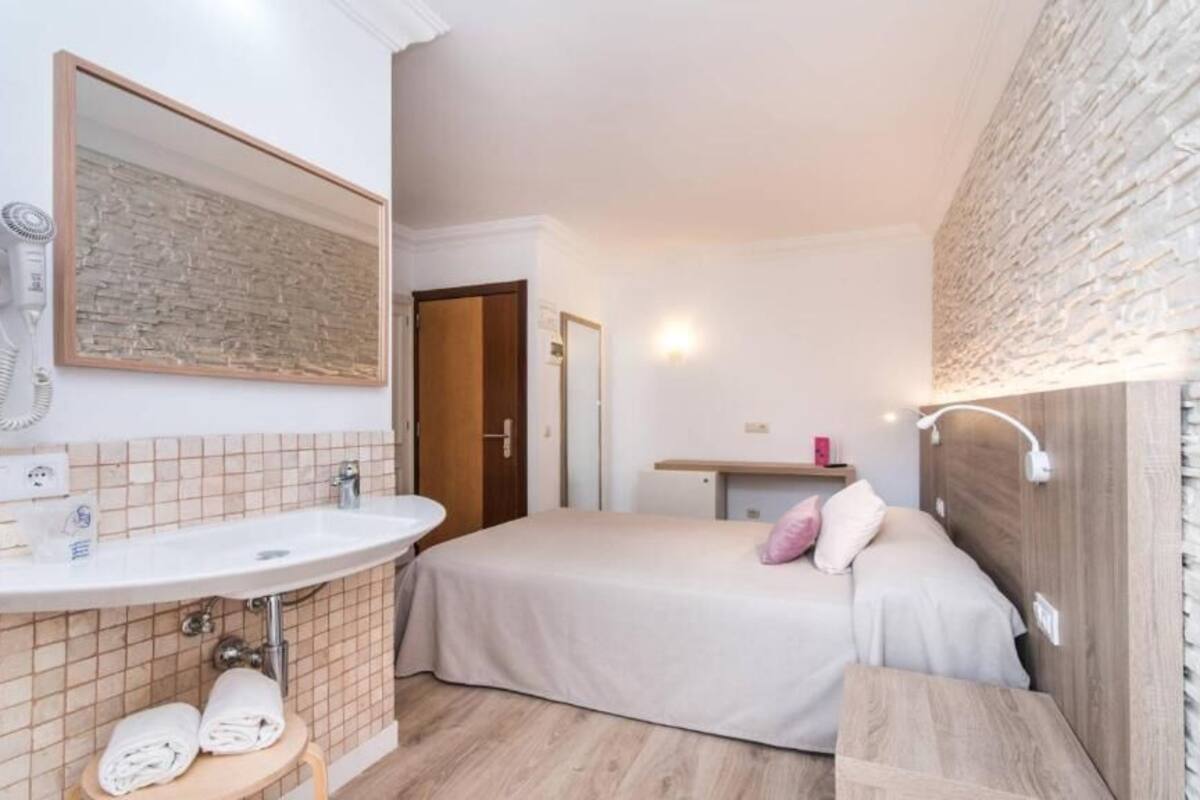 Quarto de hotel com cama, mesa de cabeceira, espelho, pia e secador de cabelo.