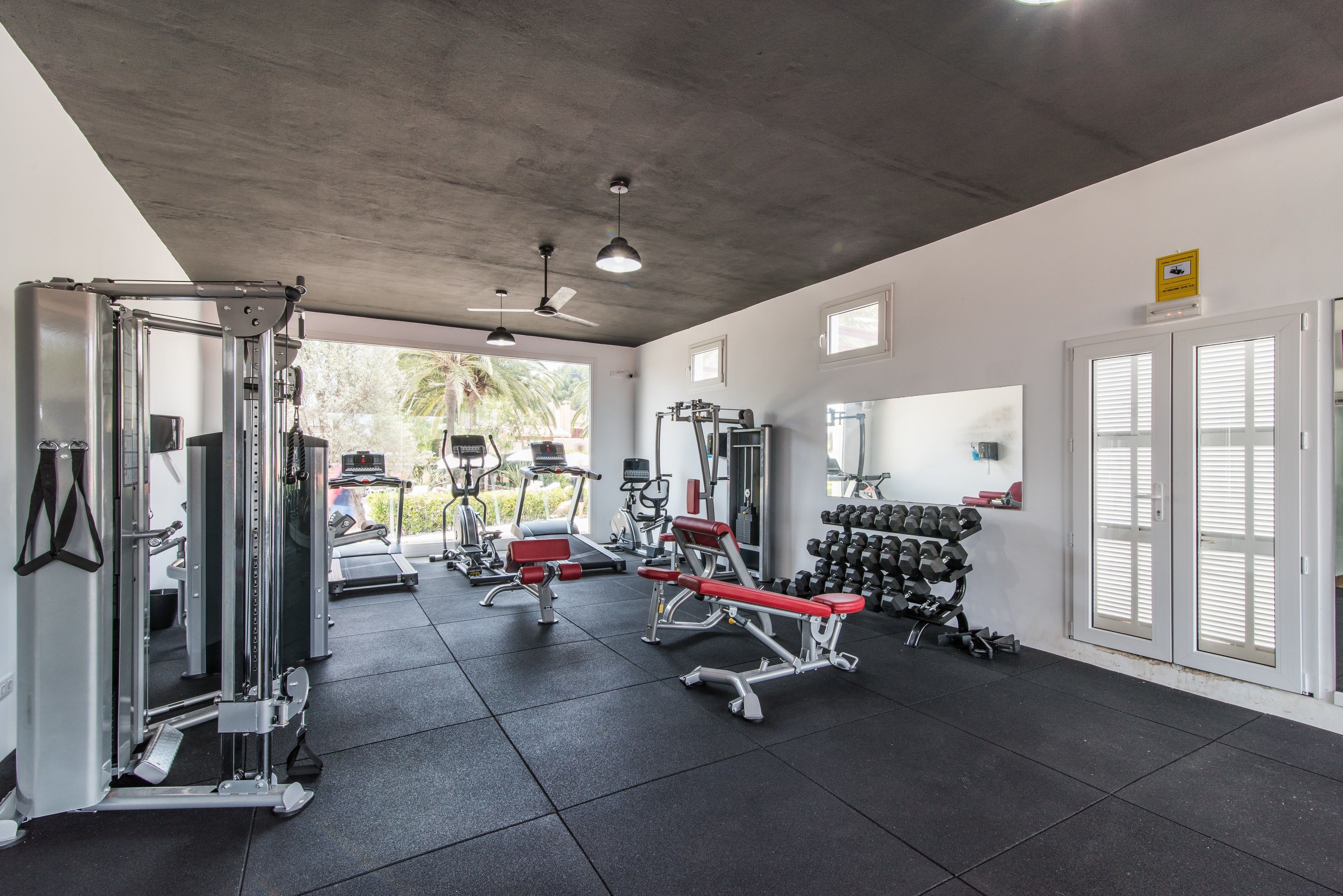 Ett gym med olika typer av träningsutrustning, en takfläkt och utsikt över omgivningen.