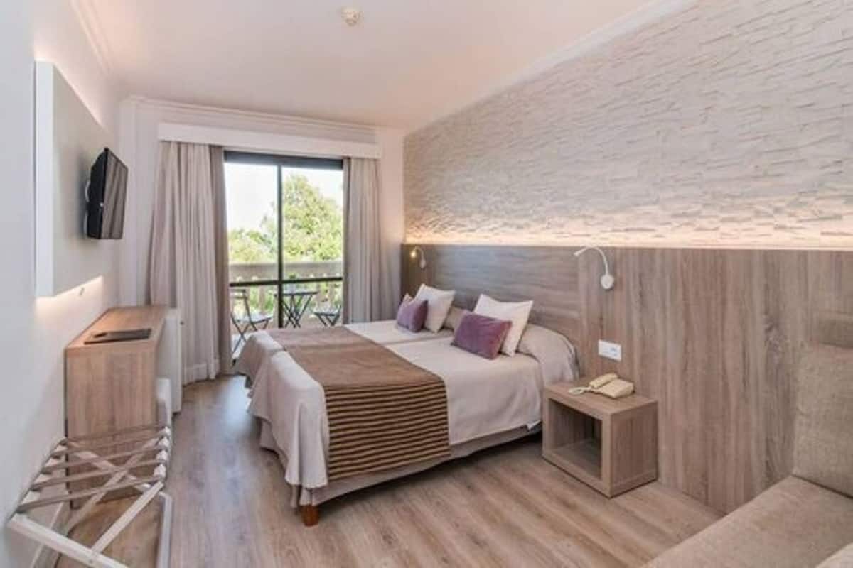 Quarto moderno com uma cama grande, cabeceira de madeira, mesa de cabeceira com abajur e vista para o exterior por uma porta deslizante.