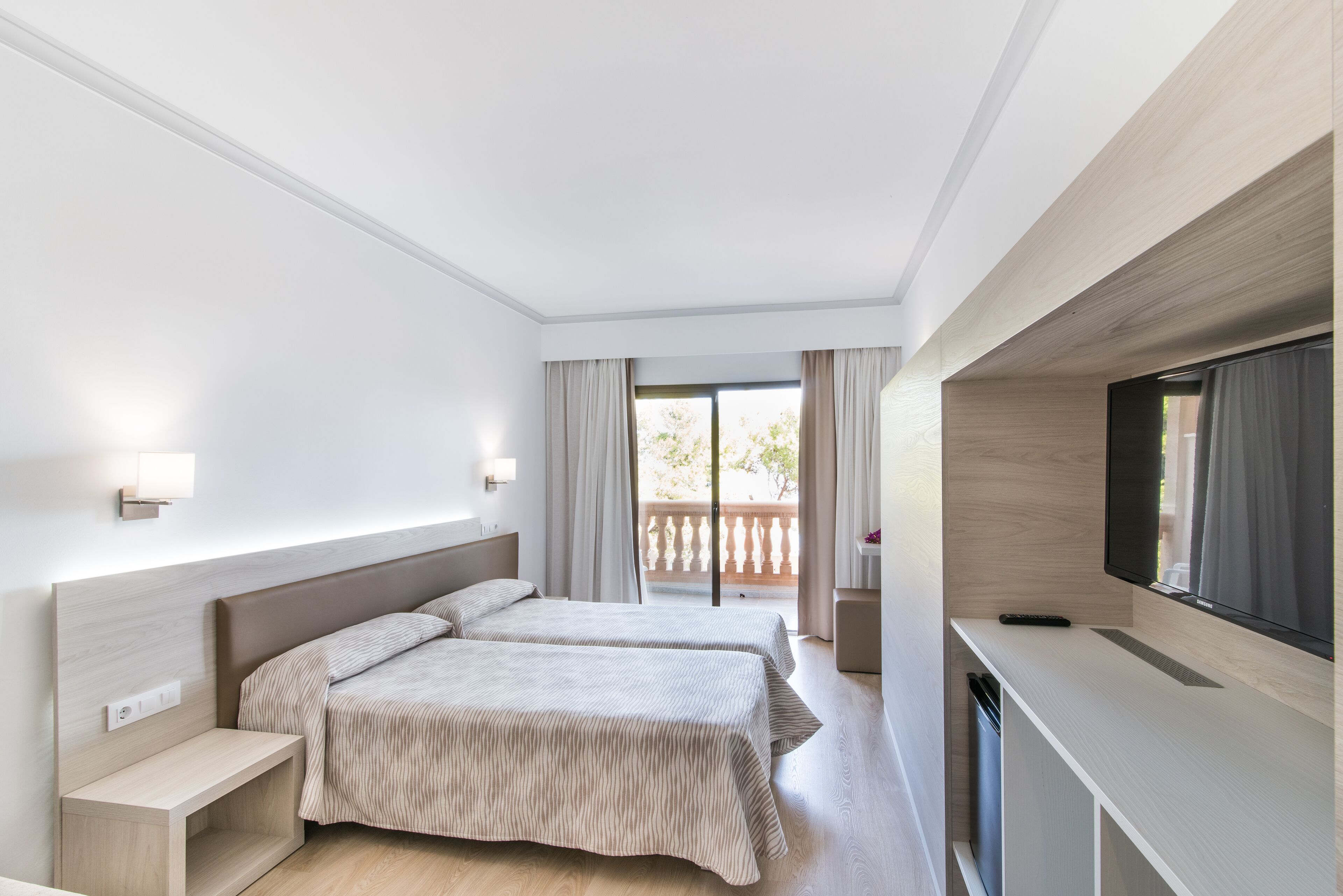 A modern hotel room with a large bed, bedside tables, a TV, and a balcony with curtains.