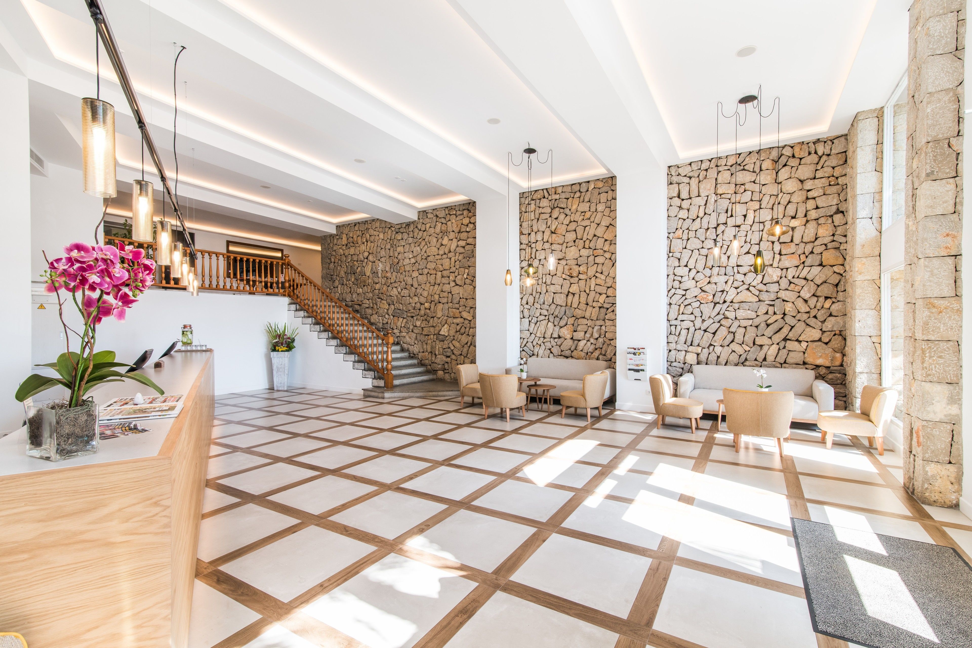 A spacious lobby with a checkered floor, a reception desk, a staircase, and stone walls.